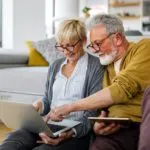 Cheerful senior couple using technology devices and having fun at home