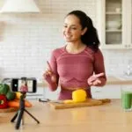 Fitness blogger lady films cooking video on smartphone in kitchen