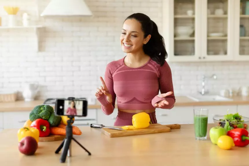 Fitness blogger lady films cooking video on smartphone in kitchen