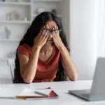 Stressed young eastern businesswoman sitting at workplace, rubbing eyes